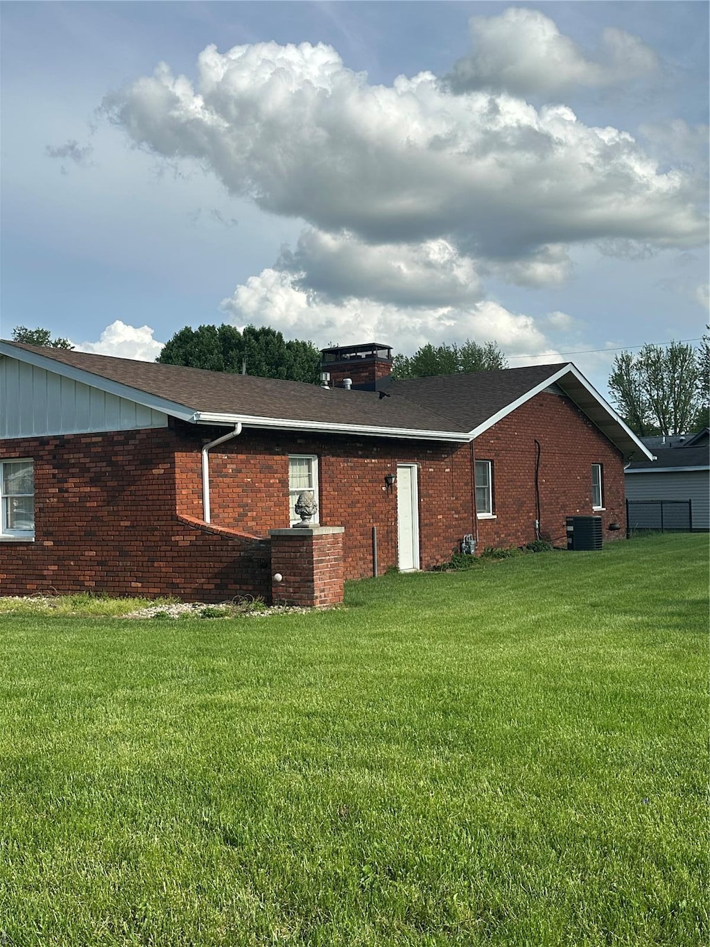 back of property featuring a lawn, cooling unit, and brick siding