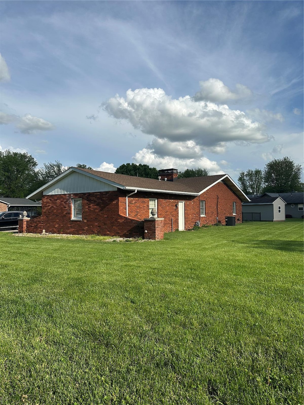 view of home's exterior with central AC unit, a chimney, a yard, and brick siding