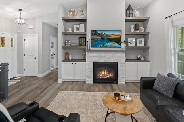 living room with baseboards, a stone fireplace, wood finished floors, and built in shelves