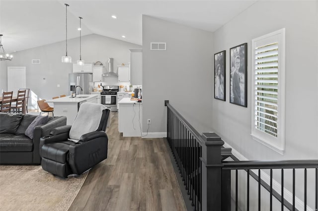 living area with visible vents, vaulted ceiling, wood finished floors, baseboards, and a chandelier