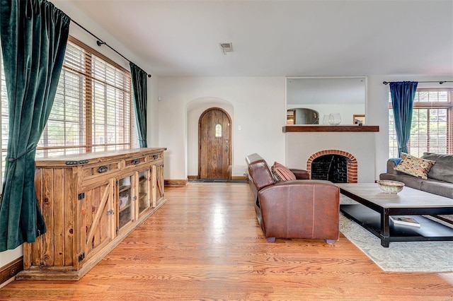 living area featuring light wood finished floors, arched walkways, a brick fireplace, and baseboards