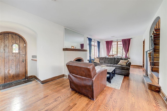 living room featuring wood finished floors, a brick fireplace, arched walkways, and plenty of natural light