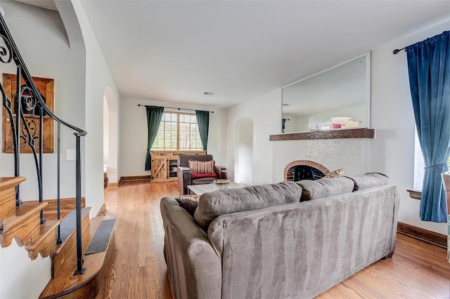 living room with arched walkways, light wood-type flooring, a brick fireplace, and stairway