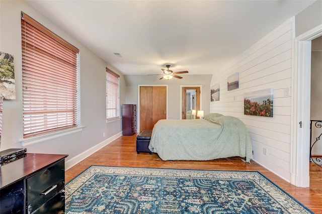 bedroom with wooden walls, wood finished floors, baseboards, and ceiling fan