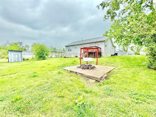 view of yard featuring an outbuilding, a deck, a storage unit, a fire pit, and fence