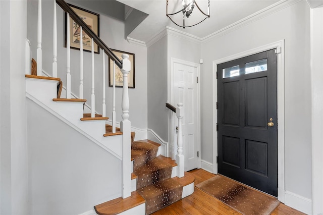 entryway featuring wood finished floors, an inviting chandelier, stairs, ornamental molding, and baseboards