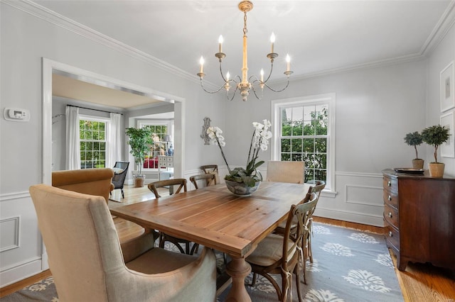 dining space with wood finished floors, an inviting chandelier, a decorative wall, wainscoting, and crown molding