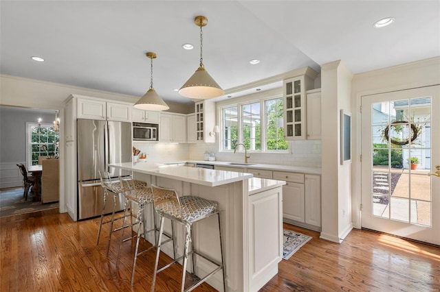 kitchen featuring stainless steel appliances, glass insert cabinets, tasteful backsplash, light countertops, and wood finished floors