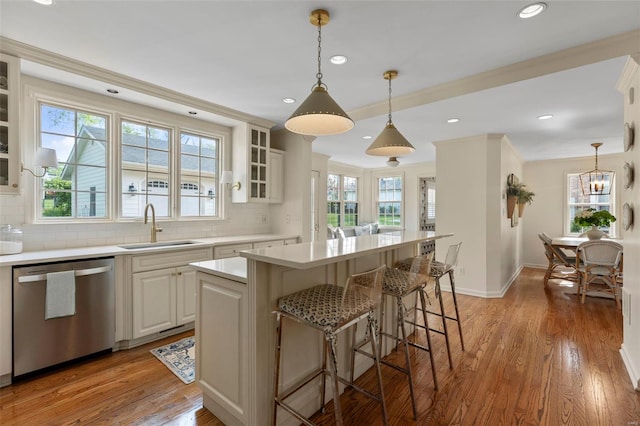 kitchen featuring stainless steel dishwasher, decorative backsplash, light countertops, a sink, and a kitchen breakfast bar