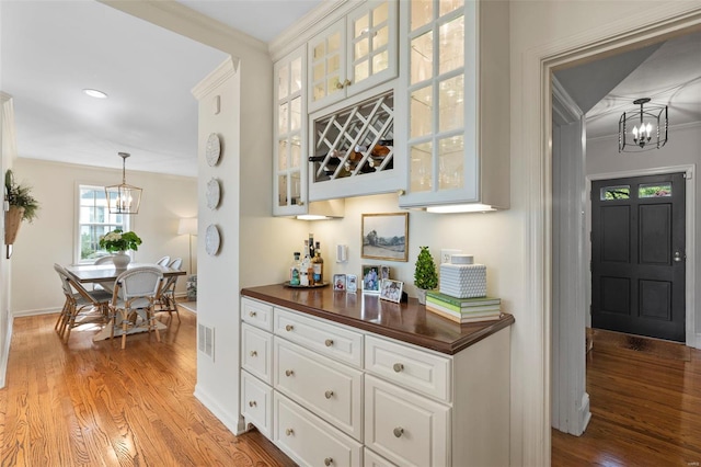 bar featuring baseboards, an inviting chandelier, crown molding, and light wood finished floors