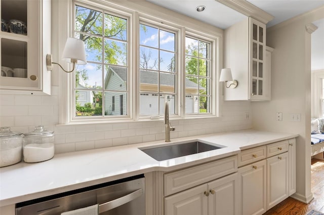 kitchen with backsplash, dishwasher, a sink, and white cabinetry
