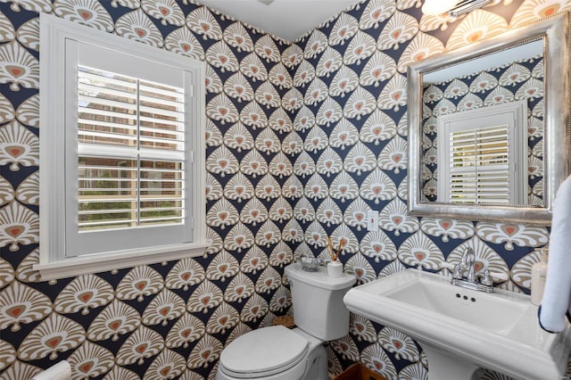 bathroom featuring toilet, wallpapered walls, and a sink