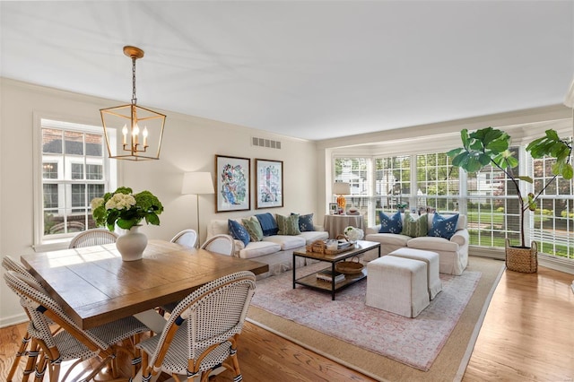 living area with ornamental molding, a notable chandelier, light wood finished floors, and visible vents
