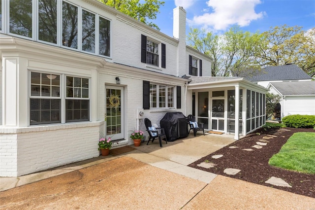 rear view of property featuring a chimney, a patio area, brick siding, and a sunroom