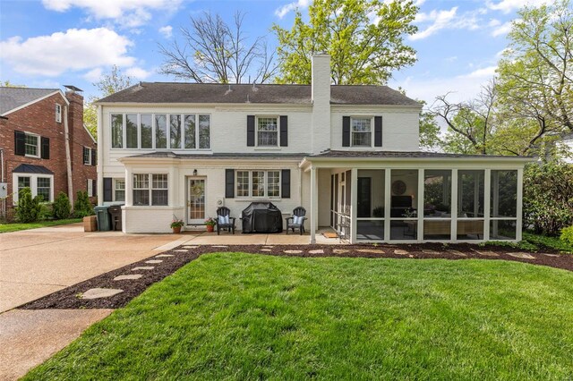 rear view of property featuring a patio, a chimney, a yard, brick siding, and a sunroom