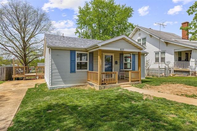 bungalow featuring concrete driveway, a shingled roof, covered porch, fence, and a front lawn