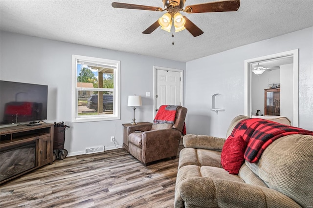 living room featuring wood finished floors, visible vents, a ceiling fan, and a textured ceiling