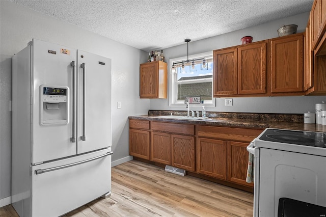 kitchen featuring a textured ceiling, a sink, visible vents, white appliances, and brown cabinetry