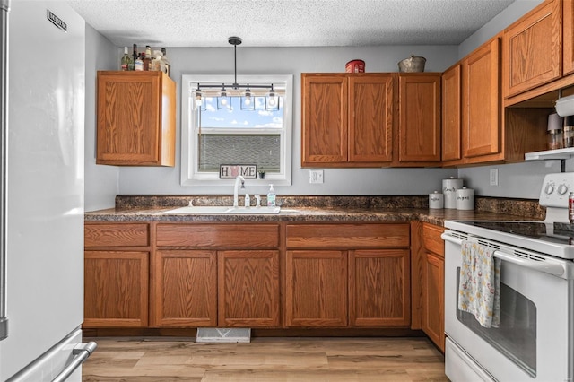 kitchen featuring brown cabinetry, a sink, electric range, and freestanding refrigerator