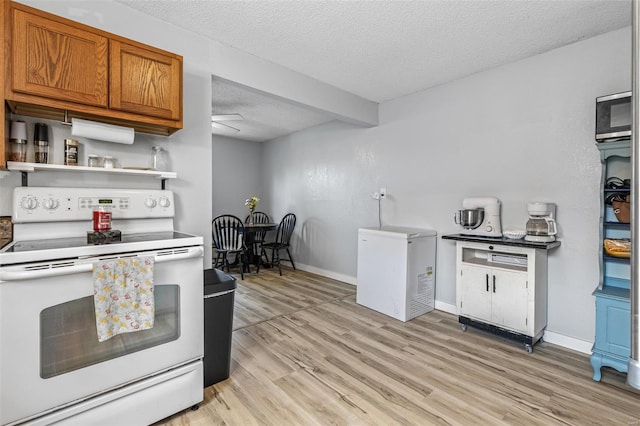 kitchen featuring white electric range oven, brown cabinetry, light wood-type flooring, refrigerator, and a textured ceiling