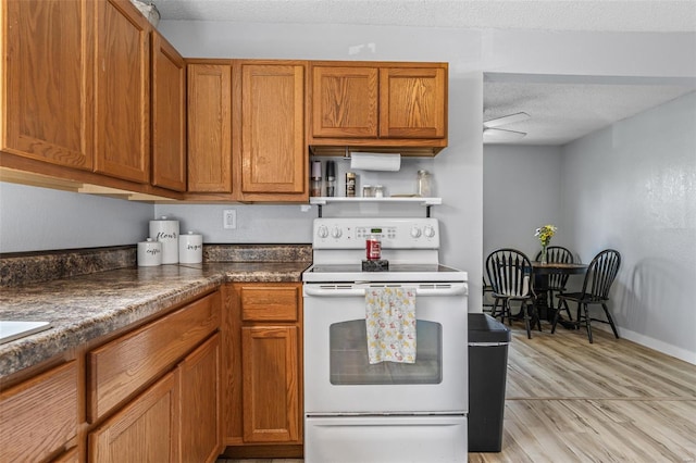 kitchen featuring a textured ceiling, brown cabinets, light wood-style flooring, dark countertops, and white electric range