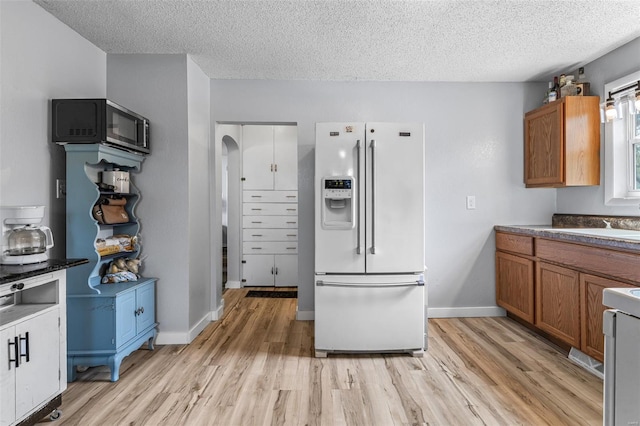 kitchen featuring white refrigerator with ice dispenser, light wood-type flooring, and brown cabinetry