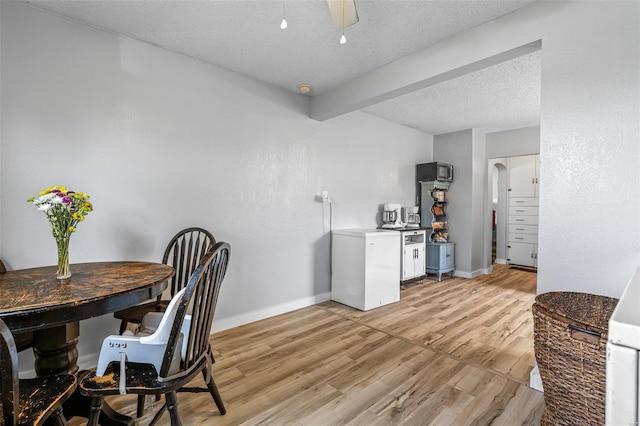 office featuring arched walkways, a ceiling fan, light wood-style flooring, baseboards, and a textured ceiling