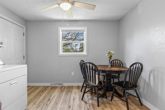 dining room with light wood finished floors, ceiling fan, baseboards, washer / clothes dryer, and a textured ceiling