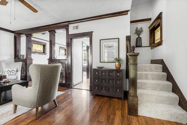 interior space featuring a ceiling fan, visible vents, crown molding, wood finished floors, and ornate columns