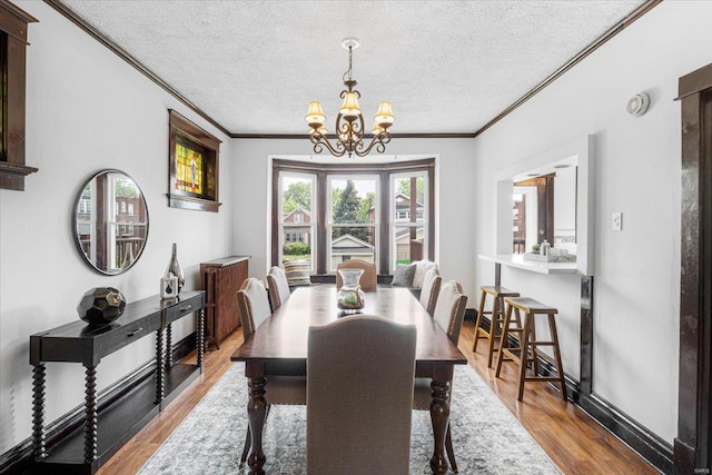 dining room with wood finished floors, ornamental molding, a textured ceiling, and a chandelier