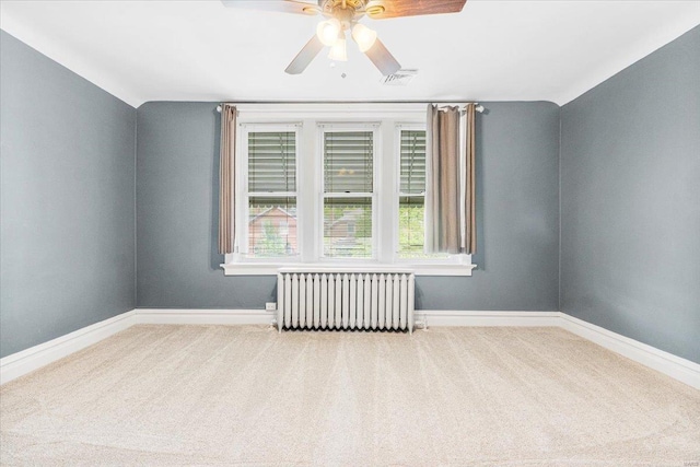 empty room with a ceiling fan, visible vents, carpet floors, baseboards, and radiator heating unit