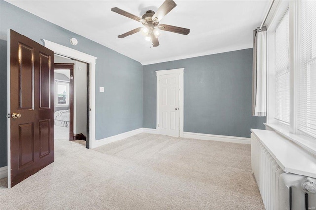 unfurnished bedroom with light colored carpet, radiator, ceiling fan, and baseboards