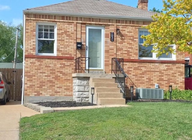 entrance to property with a lawn, brick siding, central AC, and a chimney