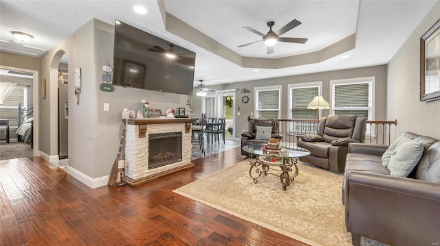 living room featuring arched walkways, ceiling fan, wood-type flooring, baseboards, and a raised ceiling