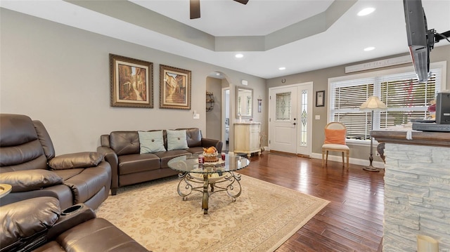 living room featuring hardwood / wood-style flooring, a raised ceiling, ceiling fan, baseboards, and arched walkways