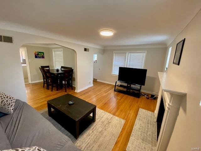 living area featuring arched walkways, visible vents, baseboards, and light wood-style floors