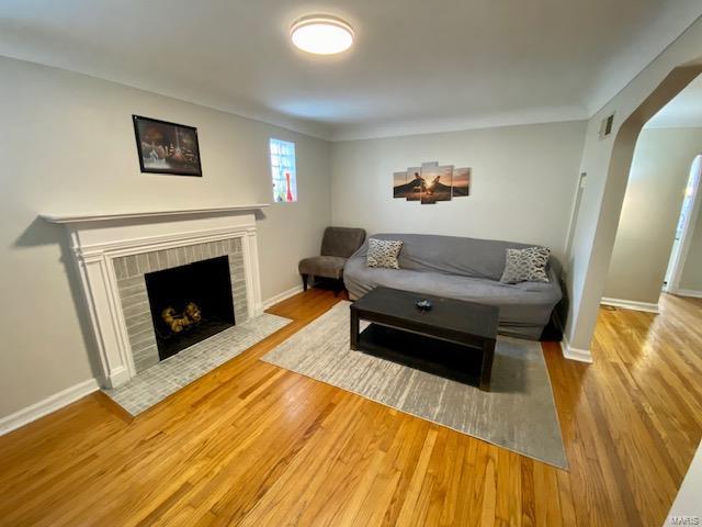 living room featuring a brick fireplace, wood finished floors, baseboards, and arched walkways