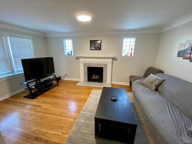 living area featuring baseboards, wood finished floors, a brick fireplace, and plenty of natural light