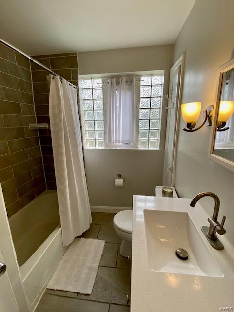 bathroom featuring a sink, baseboards, toilet, shower / bathtub combination with curtain, and tile patterned flooring