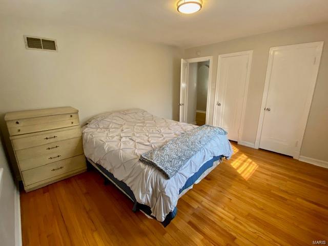 bedroom featuring wood finished floors, visible vents, two closets, and baseboards