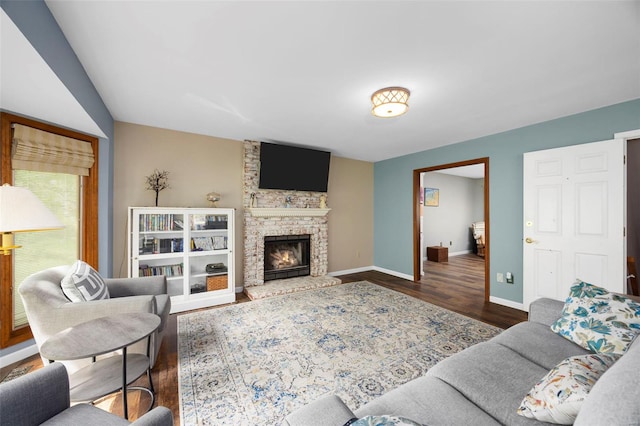 living area featuring baseboards, wood finished floors, and a stone fireplace