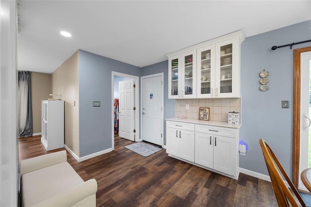 kitchen featuring decorative backsplash, glass insert cabinets, light countertops, dark wood-type flooring, and baseboards