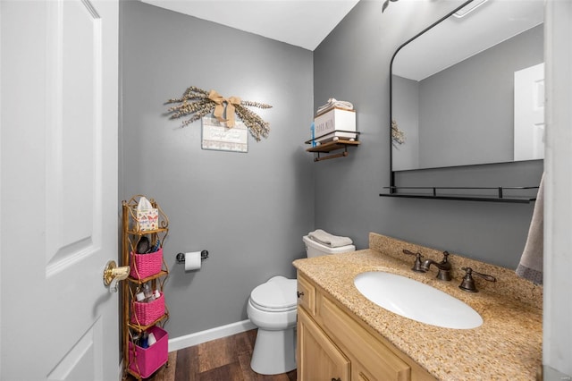 half bath featuring baseboards, wood finished floors, toilet, and vanity