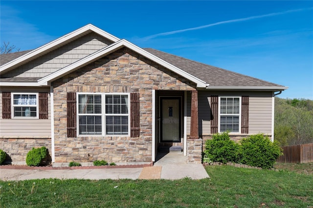 craftsman-style house featuring fence, roof with shingles, a front yard, and stone siding