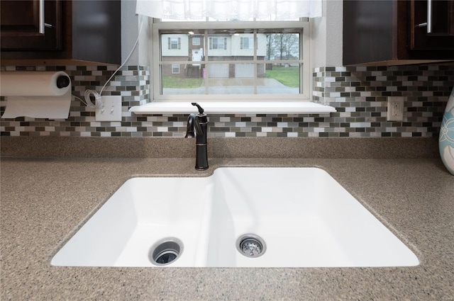 interior details with light stone countertops, a sink, backsplash, and dark brown cabinetry
