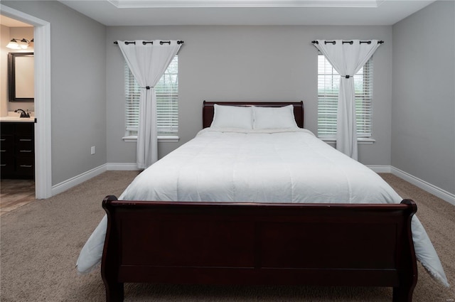 carpeted bedroom with baseboards, ensuite bath, and a sink