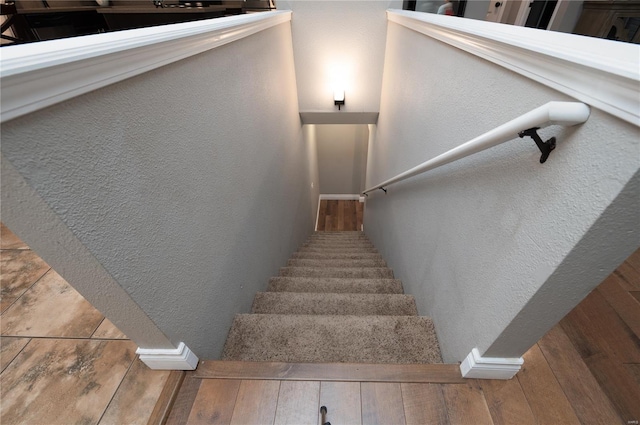 stairs with wood finished floors and a textured wall