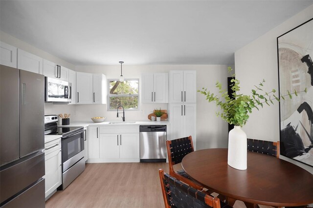 kitchen with appliances with stainless steel finishes, a sink, light countertops, light wood-style floors, and white cabinetry