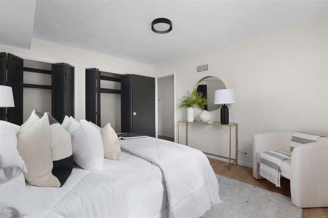 bedroom featuring baseboards, multiple closets, visible vents, and wood finished floors