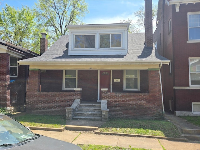 bungalow-style house featuring a chimney, brick siding, a porch, and a shingled roof